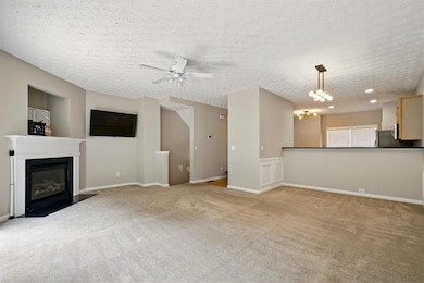 Unfurnished living room with light colored carpet, a fireplace with flush hearth, a ceiling fan, a textured ceiling, and a chandelier