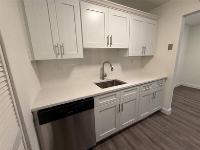 Kitchen featuring stainless steel dishwasher, dark wood-style floors, backsplash, and white cabinetry