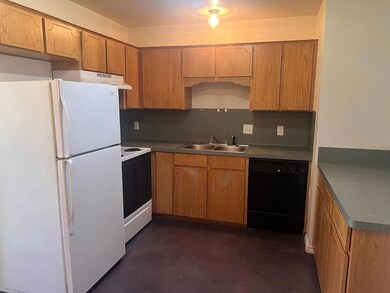 Kitchen with white appliances, decorative backsplash, brown cabinetry, concrete flooring, and dark countertops