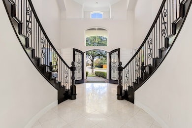 A grand entryway featuring a dramatic dual staircase, wrought iron detailing, and elegant tile flooring creates an unforgettable first impression as you step through the custom double doors.