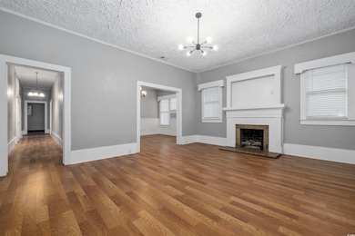 Unfurnished living room with a textured ceiling, a notable chandelier, and dark wood-type flooring