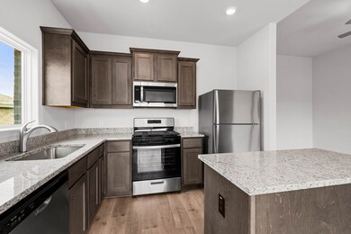 Kitchen featuring appliances with stainless steel finishes, light stone counters, light wood-style floors, dark brown cabinetry, and a center island