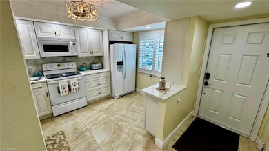 Kitchen featuring white appliances, light countertops, decorative backsplash, recessed lighting, and a chandelier
