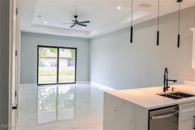 Kitchen featuring light marble finish flooring, a tray ceiling, stainless steel dishwasher, white cabinets, and ceiling fan