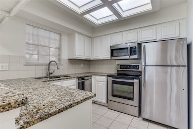 Kitchen with stainless steel appliances, light stone counters, white cabinets, decorative backsplash, and light tile patterned floors