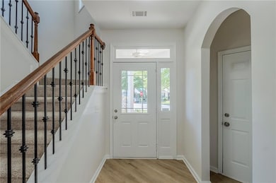 Foyer entrance featuring light wood-style floors, arched walkways, baseboards, and stairs