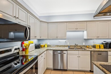 Kitchen with stainless steel appliances, a sink, crown molding, light tile patterned floors, and light stone countertops
