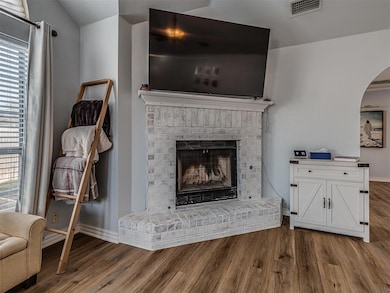 Living room featuring visible vents, baseboards, a fireplace, wood finished floors, and arched walkways