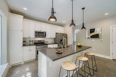 Kitchen featuring tasteful backsplash, stainless steel appliances, a kitchen breakfast bar, white cabinets, and decorative light fixtures