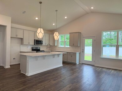 Kitchen featuring appliances with stainless steel finishes, a sink, lofted ceiling, backsplash, and a center island with sink