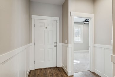 Hall featuring dark wood-style floors, a wainscoted wall, and a decorative wall