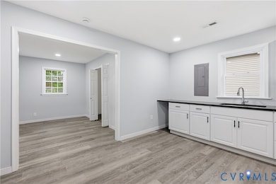 Kitchen with light wood finished floors, electric panel, white cabinets, recessed lighting, and dark countertops