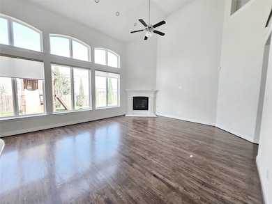 Unfurnished living room with high vaulted ceiling, dark wood-style floors, a glass covered fireplace, and a ceiling fan