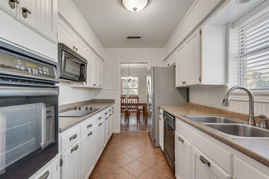 Kitchen with black appliances, white cabinetry, ornamental molding, light tile patterned flooring, and light countertops
