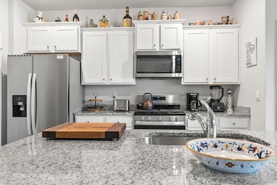 Kitchen with stainless steel appliances, white cabinetry, and light stone countertops