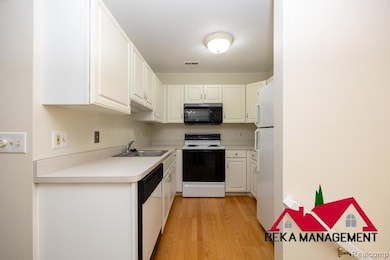 Kitchen with white appliances, light wood finished floors, white cabinetry, and light countertops