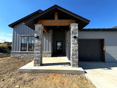 Entrance to property with stone siding, covered porch, concrete driveway, an attached garage, and board and batten siding