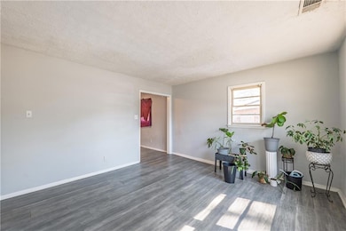 Spare room featuring dark wood-type flooring, baseboards, visible vents, and a textured ceiling