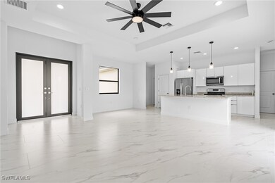 Unfurnished living room with a tray ceiling, a ceiling fan, recessed lighting, light marble finish flooring, and french doors
