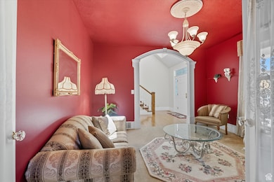 Carpeted living room with arched walkways, stairs, decorative columns, and a chandelier