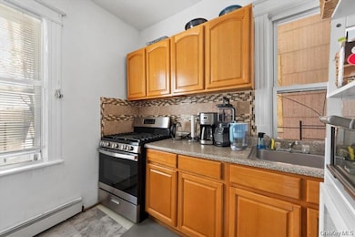 Kitchen featuring white appliances, baseboard heating, tasteful backsplash, and brown cabinetry