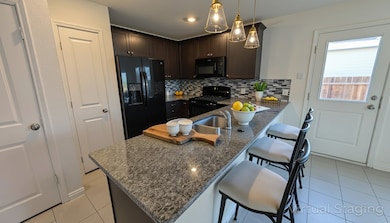Kitchen featuring a peninsula, a kitchen breakfast bar, decorative backsplash, black appliances, and dark brown cabinetry