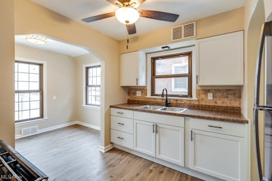 Kitchen featuring light hardwood / wood-style floors, ceiling fan, backsplash, white cabinets, and sink