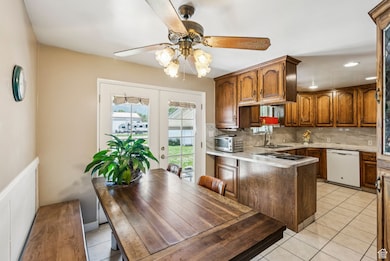 Kitchen featuring tasteful backsplash, french doors, a peninsula, light tile patterned floors, and white dishwasher