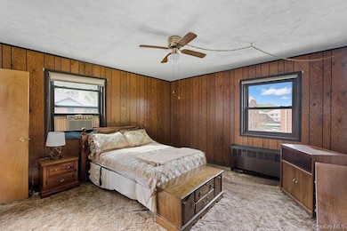 Bedroom with radiator heating unit, multiple windows, light carpet, and wooden walls