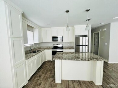 Kitchen with stainless steel appliances, a center island, dark wood-type flooring, white cabinetry, and light stone countertops