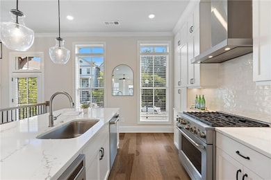 Kitchen with wall chimney exhaust hood, stainless steel appliances, ornamental molding, dark wood finished floors, and light stone counters