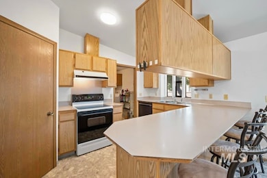 Kitchen featuring electric range oven, a kitchen bar, a peninsula, light countertops, and light brown cabinets