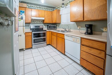 Kitchen with appliances with stainless steel finishes, light countertops, light tile patterned floors, vaulted ceiling, and under cabinet range hood
