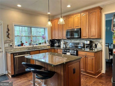 Kitchen with stainless steel appliances, a sink, backsplash, dark stone counters, and dark wood-style floors