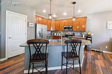 Kitchen featuring stainless steel appliances, brown cabinets, dark wood-style floors, decorative light fixtures, and a kitchen breakfast bar