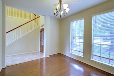 This room features hardwood flooring, large windows with blinds allowing natural light, neutral wall colors, and a modern overhead light fixture, creating a bright and welcoming space.