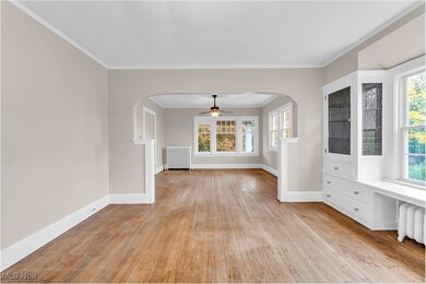 Spare room featuring arched walkways, a ceiling fan, light wood-style floors, radiator heating unit, and ornamental molding
