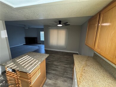 Kitchen featuring ceiling fan, a textured ceiling, a brick fireplace, light stone countertops, and open floor plan