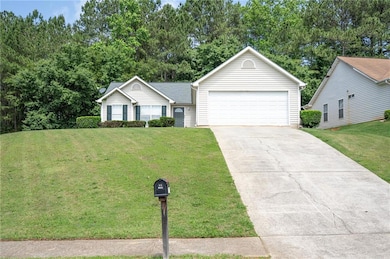 Ranch-style home featuring a garage, a front lawn, and view of wooded area