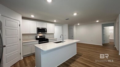 Kitchen featuring dark vinyl / wood-style floors, stainless steel appliances, white cabinetry, and a kitchen island with sink
