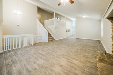 Unfurnished living room featuring a ceiling fan, vaulted ceiling, wood finished floors, baseboards, and a chandelier