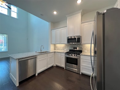 Kitchen with appliances with stainless steel finishes, white cabinetry, dark wood finished floors, light stone countertops, and recessed lighting
