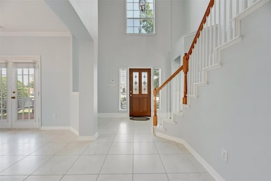 Foyer entrance featuring light tile patterned floors, french doors, stairs, crown molding, and a high ceiling