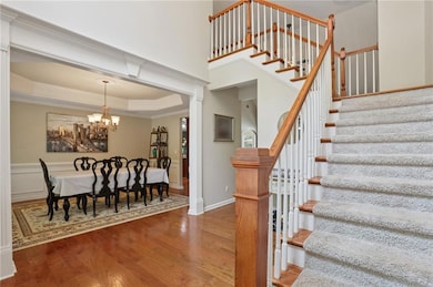 Stairs featuring a chandelier, wood finished floors, ornamental molding, a raised ceiling, and baseboards