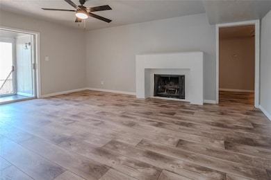 Unfurnished living room featuring wood finished floors, ceiling fan, baseboards, and a tiled fireplace