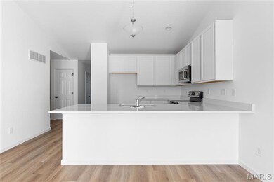 Kitchen featuring white cabinetry, light wood finished floors, a peninsula, appliances with stainless steel finishes, and decorative light fixtures