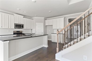 Kitchen with stainless steel appliances, dark countertops, crown molding, white cabinetry, and dark wood-type flooring