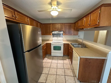 Kitchen featuring white appliances, a sink, under cabinet range hood, light countertops, and brown cabinetry