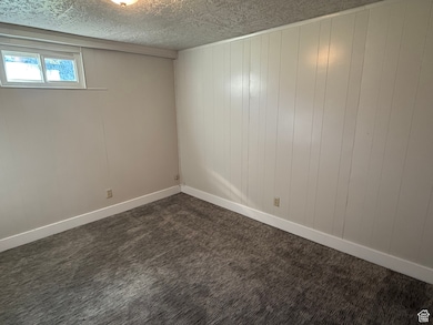 Spare room with dark colored carpet, wood walls, and a textured ceiling