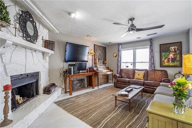 Living area featuring ceiling fan, a stone fireplace, and a textured ceiling